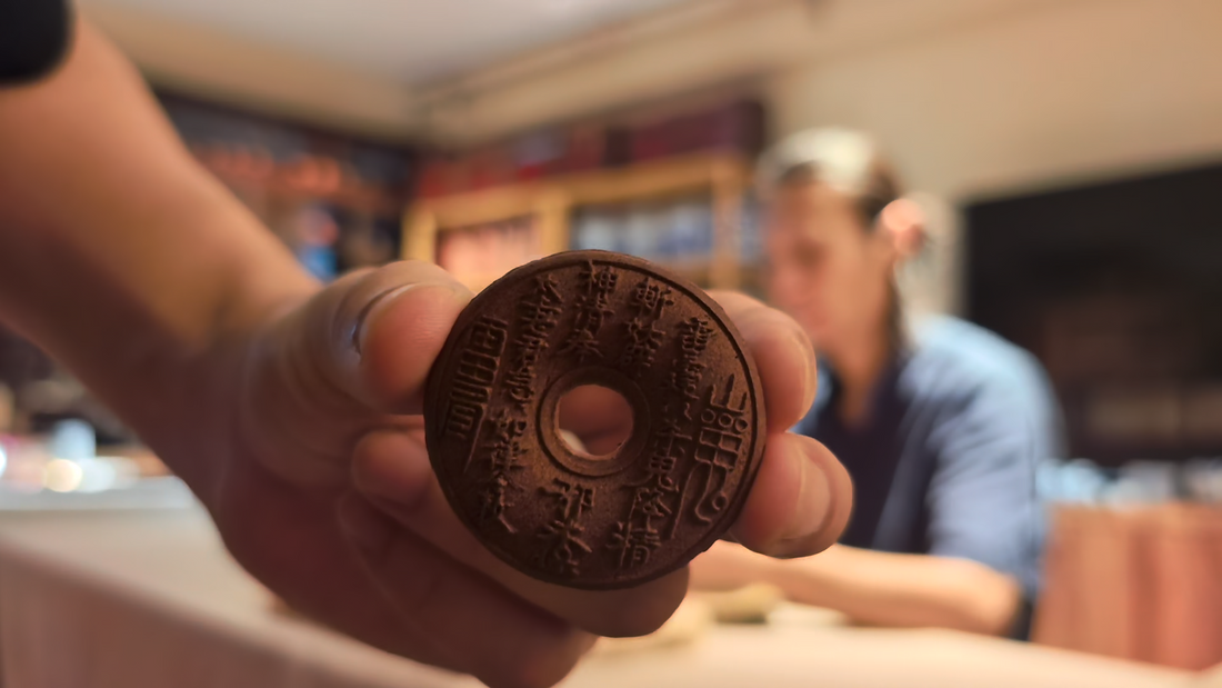 Close-up of a hand holding a circular carved incense plaque in the workshop